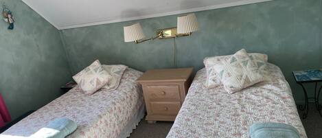 Een slaapkamer met twee eenpersoonsbedden, een nachtkastje, een lamp en een klein tafeltje.