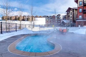 A heated outdoor pool with a curved edge, surrounded by a paved walkway and a metal fence.