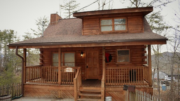 A wooden cabin with a porch, a front door, and a small window.