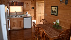 A wooden cabin interior with a kitchen, dining table, and chairs.