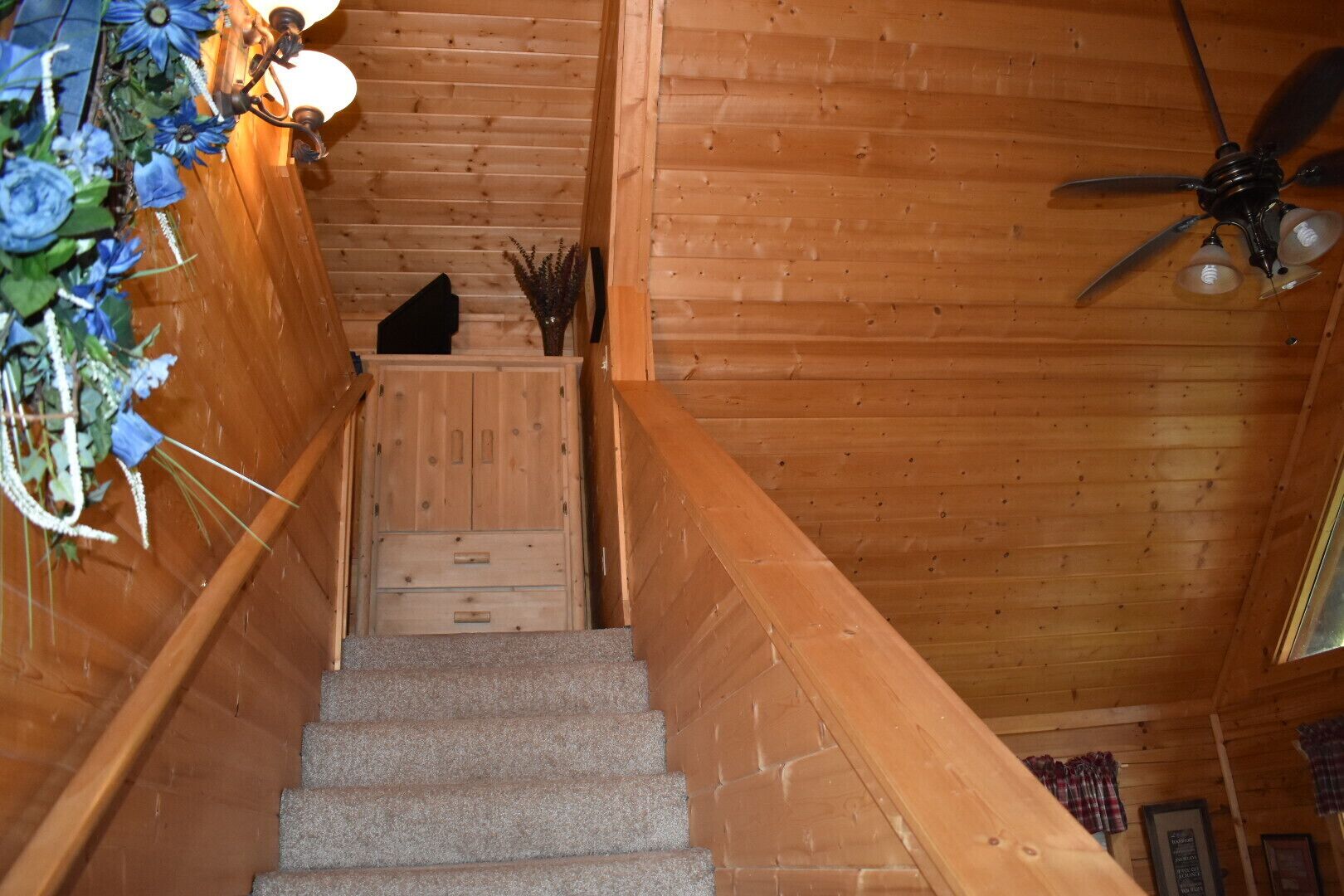 A wooden staircase with a ceiling fan, a decorative wall with flowers, and a small table with a vase.
