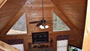 A wooden cabin with a fireplace, a ceiling fan, and a television.