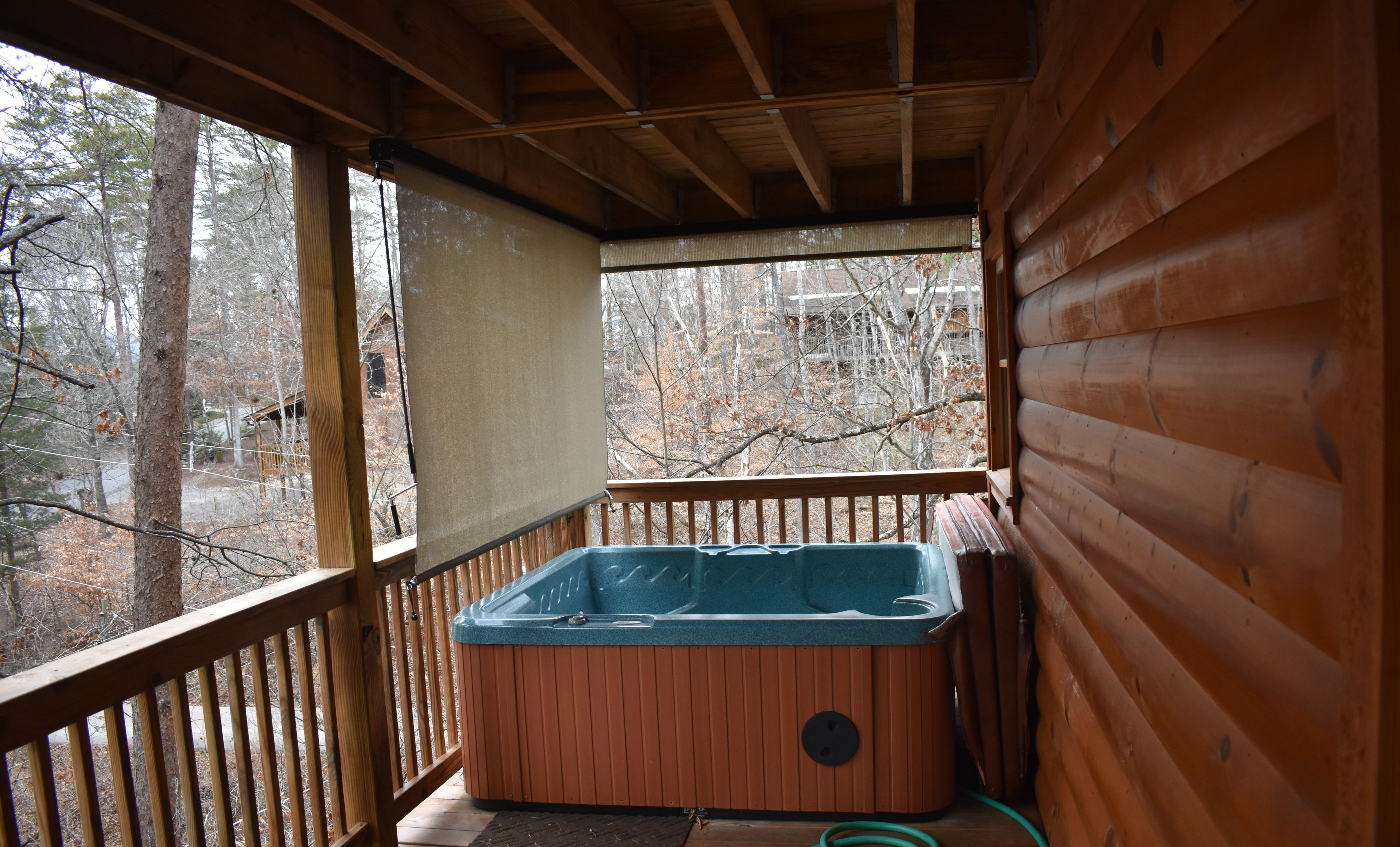 A wooden deck with a hot tub, a wooden railing, and a view of trees.