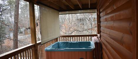 A wooden deck with a hot tub, a wooden railing, and a view of trees.