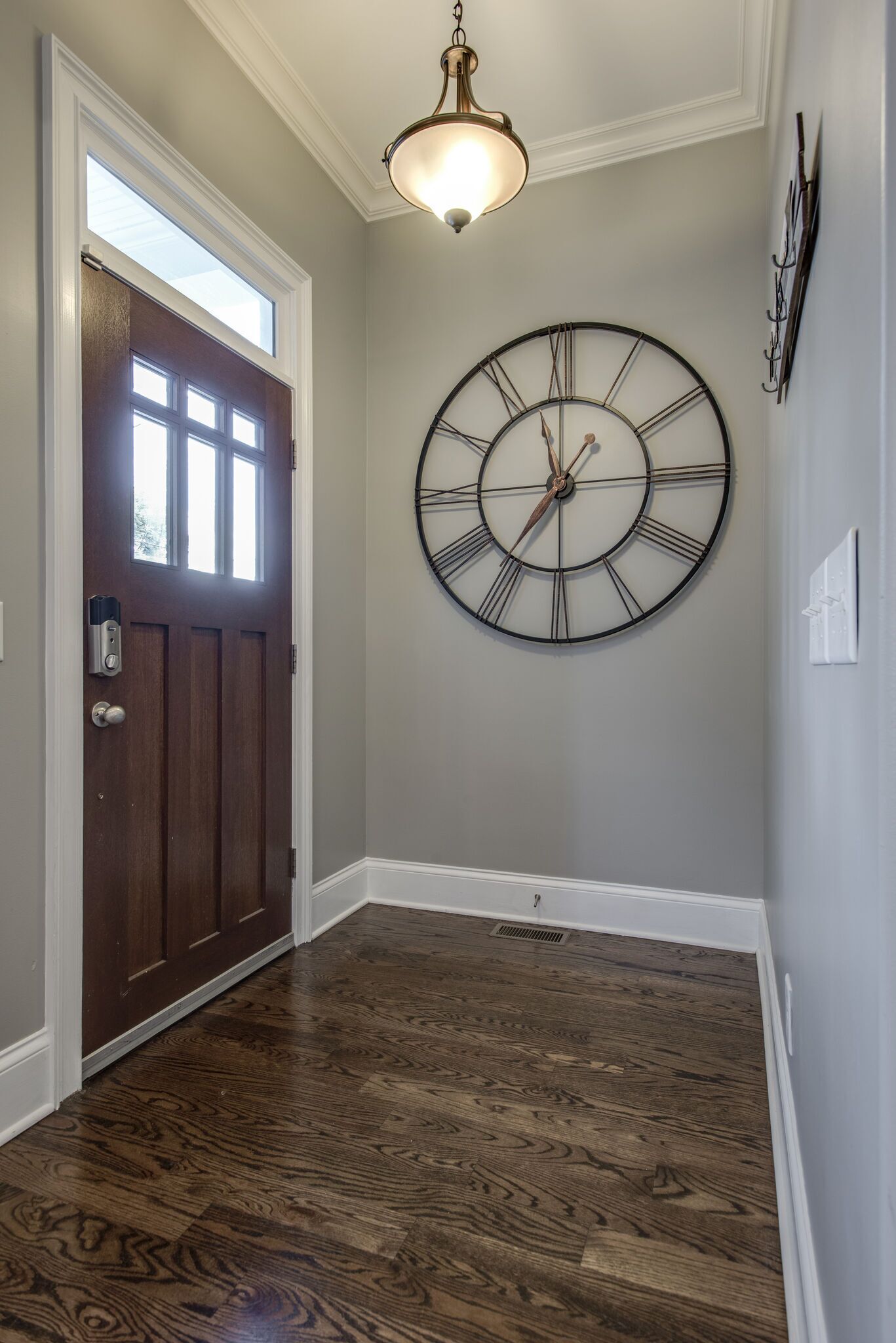 Un couloir avec une porte en bois, une grande horloge murale et un luminaire au plafond.