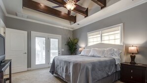 Quarto com cama, mesa de cabeceira, abajur, ventilador de teto e porta.