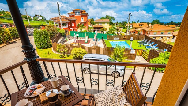 Un balcon avec une table préparée pour le petit-déjeuner, une vue sur une piscine et les maisons environnantes.