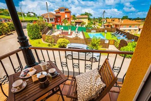 Un balcón con una mesa dispuesta para el desayuno, vista a una piscina y casas circundantes.