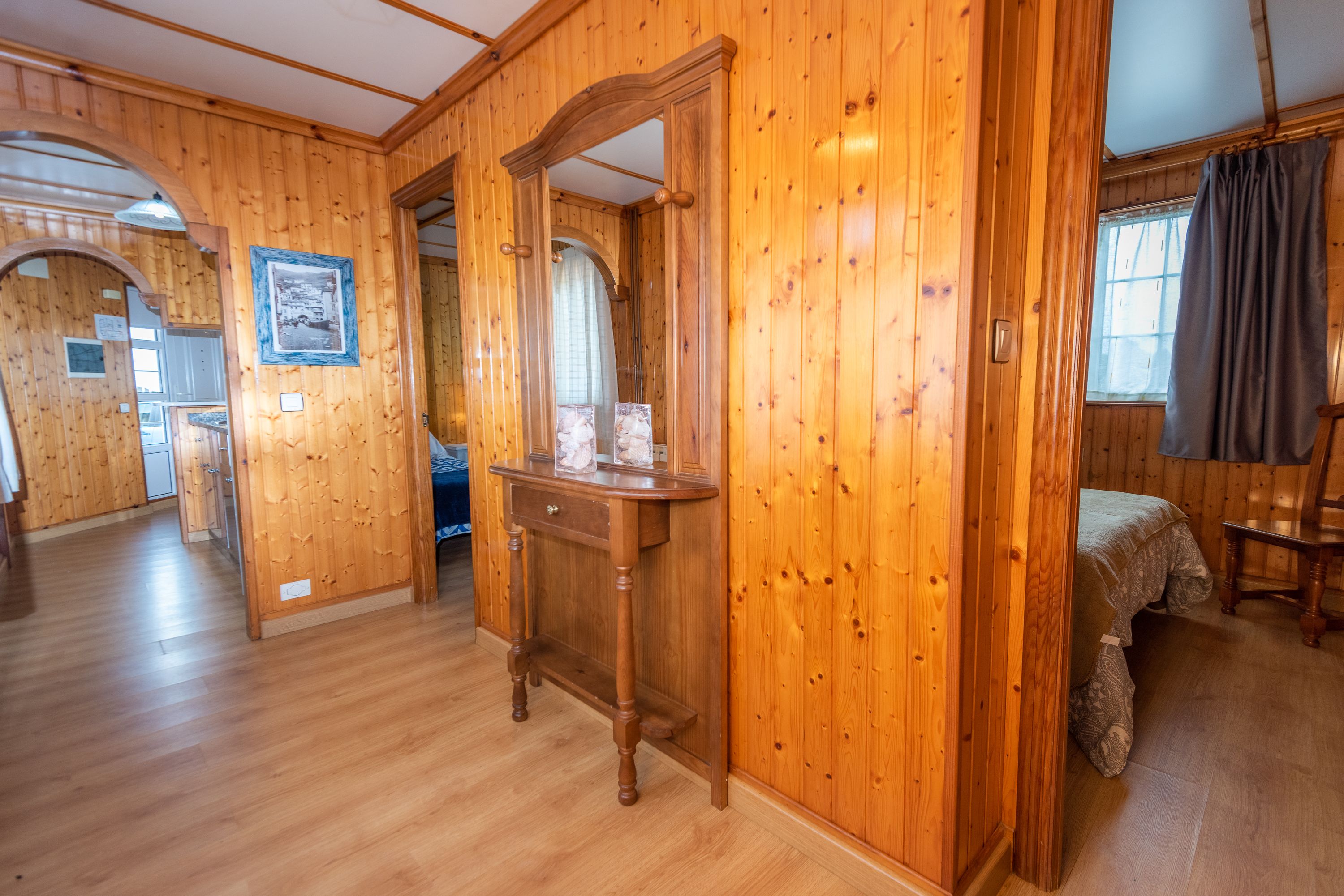 Ein Zimmer mit Holzwänden, einem Bett, einer Holzkommode und einem Spiegel.