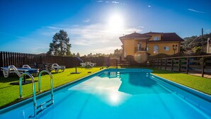 Une piscine avec une terrasse en bois, une maison en arrière-plan et un ciel dégagé.