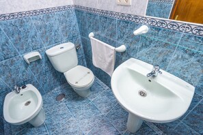 Un baño con piso de azulejos azules, inodoro, bidé y lavamanos.