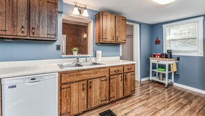 A kitchen with wooden cabinets, a dishwasher, a sink, and a small cart with kitchen items. - Amazing historic home from 1860!  (St Charles)