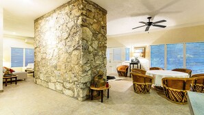 A room with a stone pillar, a ceiling fan, wicker chairs, a round table, and a window with blue shutters. - BIG! 3BR Home Fully Equipped, Pool, Gardens & WiFi (El Cedral)