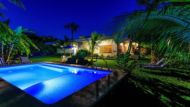 A swimming pool with lounge chairs and umbrellas, surrounded by tropical plants and a house in the background. - BIG! 3BR Home Fully Equipped, Pool, Gardens & WiFi (El Cedral)