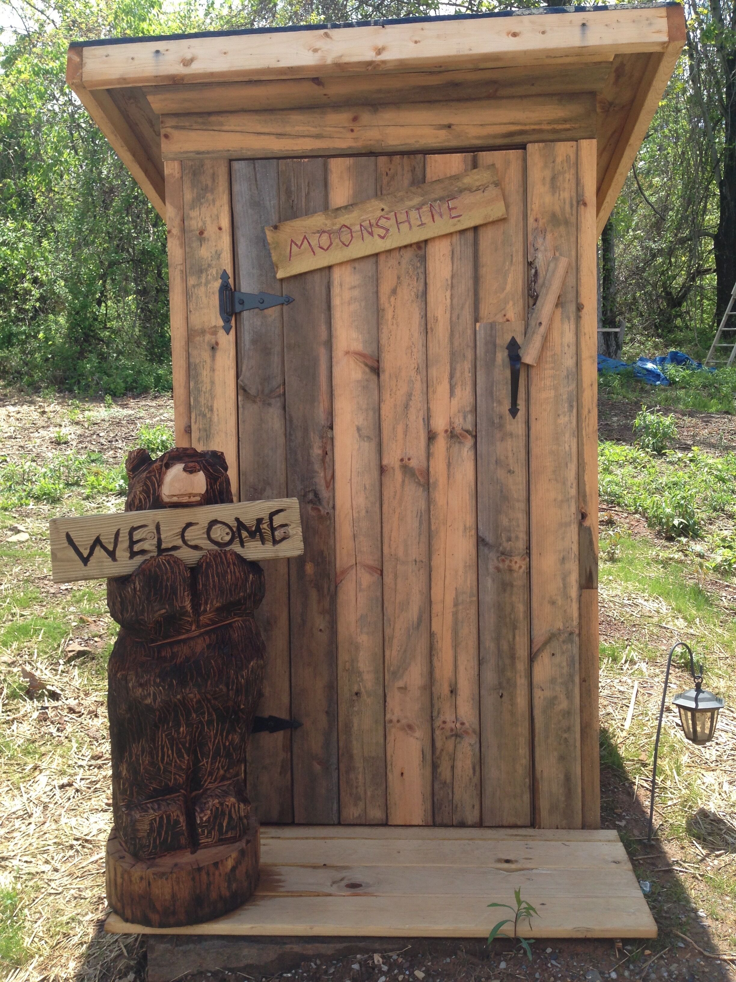 Une cabane en bois avec une pancarte « Bienvenue » et une autre pancarte « Moonshine » sur la porte.