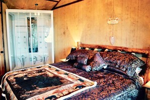 Ein Schlafzimmer mit Holz-Kopfende, einem großen Bett mit gemusterten Betttextilien, einem beleuchteten Spiegel und einer Tür mit einem Schild.