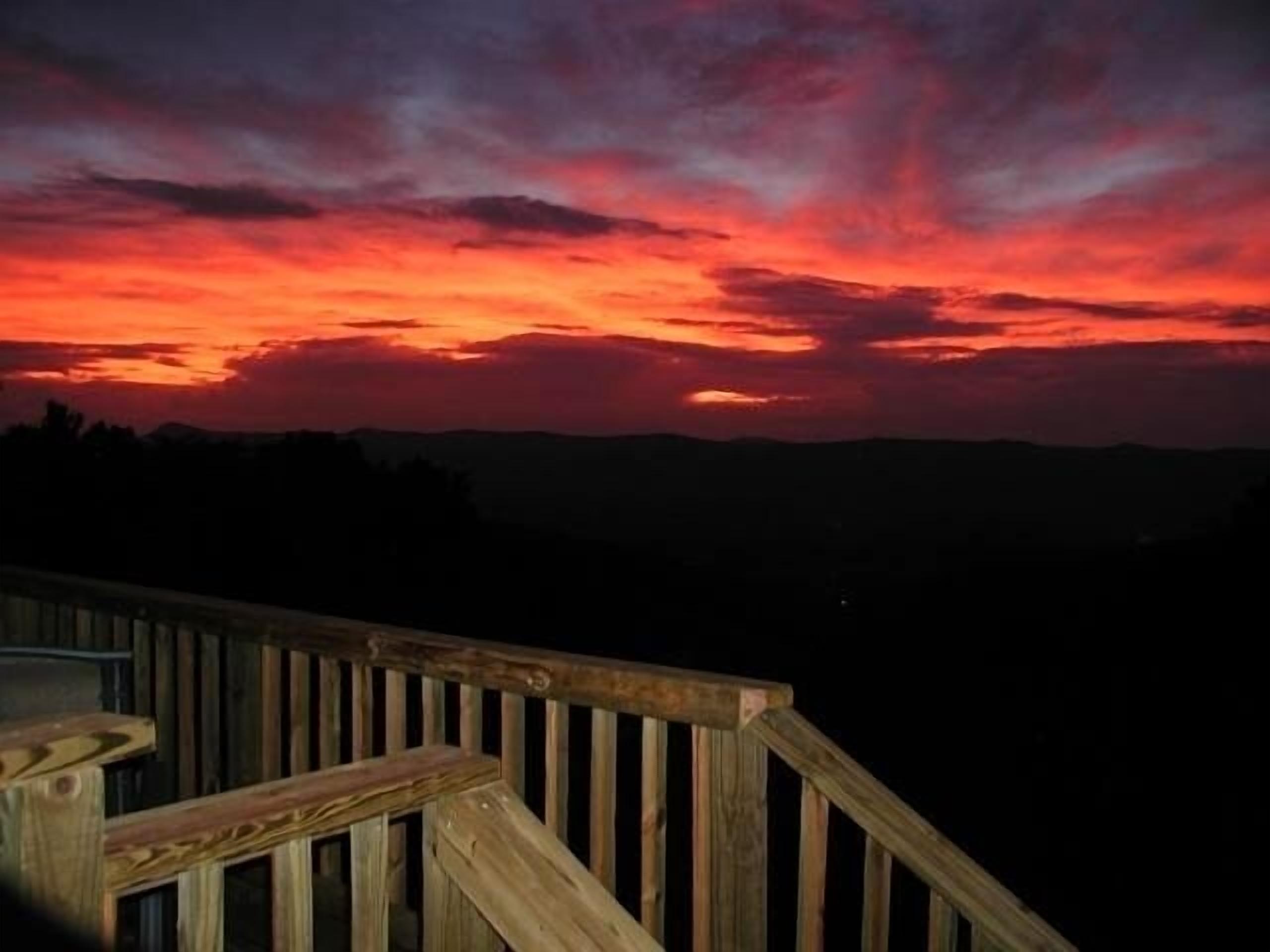 Eine Holzterrasse mit Geländer, die auf eine Landschaft im Abendlicht blickt.