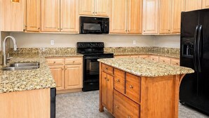 A kitchen with wooden cabinets, a granite countertop, a black refrigerator, and a microwave. - Centrally Located- 2 mi. North of downtown OS with screened porch, full kitchen (Ocean Springs)