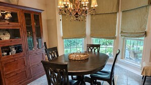 A dining room with a round table, dark chairs, a chandelier, and a cabinet with glass doors. - Centrally Located- 2 mi. North of downtown OS with screened porch, full kitchen (Ocean Springs)