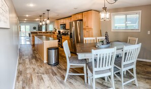 Une cuisine moderne avec des meubles en bois, des appareils en acier inoxydable et un coin repas avec des chaises blanches.