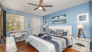 Un dormitorio con cama, escritorio, silla y ventilador de techo.