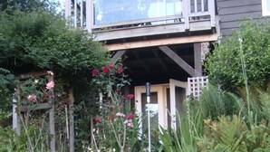 Ein Garten mit verschiedenen Blumen und Pflanzen, eine Holzterrasse und ein Haus mit Balkon.
