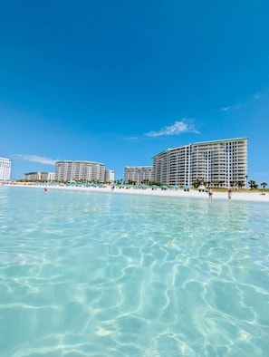 A beachfront hotel with multiple high-rise buildings, clear blue water, and a sandy beach.