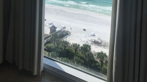 A view of the ocean through a window with curtains, a sandy beach, and a small building structure. - Newly Renovated Gulf Front Gorgeous Views in St. Maarten from the 10th floor!  (Destin)