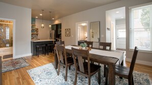 A dining area with a wooden table, chairs, and a rug. There is a kitchen in the background with a counter and stools. - Family Friendly Modern Historic Luxury, Minutes to Walk to CSU and Old Town!  (Fort Collins)