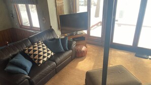 A living room with a leather sofa, a flat-screen TV, a coffee table, and a large window.