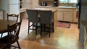 A kitchen with wooden cabinets, a dining table with chairs, a hanging light fixture, and a window with a view of trees.