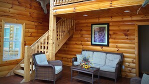 A log cabin interior with a wooden staircase, wicker furniture, a framed picture, and a large animal hide on the wall. - Great for family vacations, weddings, And Church retreats.  (Fort Payne)