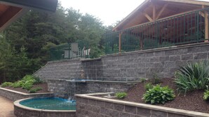 A stone retaining wall with a small waterfall feature, a circular pool, and a wooden deck area. - Great for family vacations, weddings, And Church retreats.  (Fort Payne)