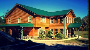 A large log cabin with a green roof, multiple windows, and a covered porch area. - Great for family vacations, weddings, And Church retreats.  (Fort Payne)