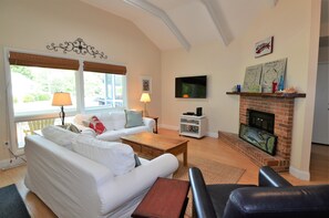 Una sala de estar con chimenea, sofás blancos, televisor y pared de ladrillo.