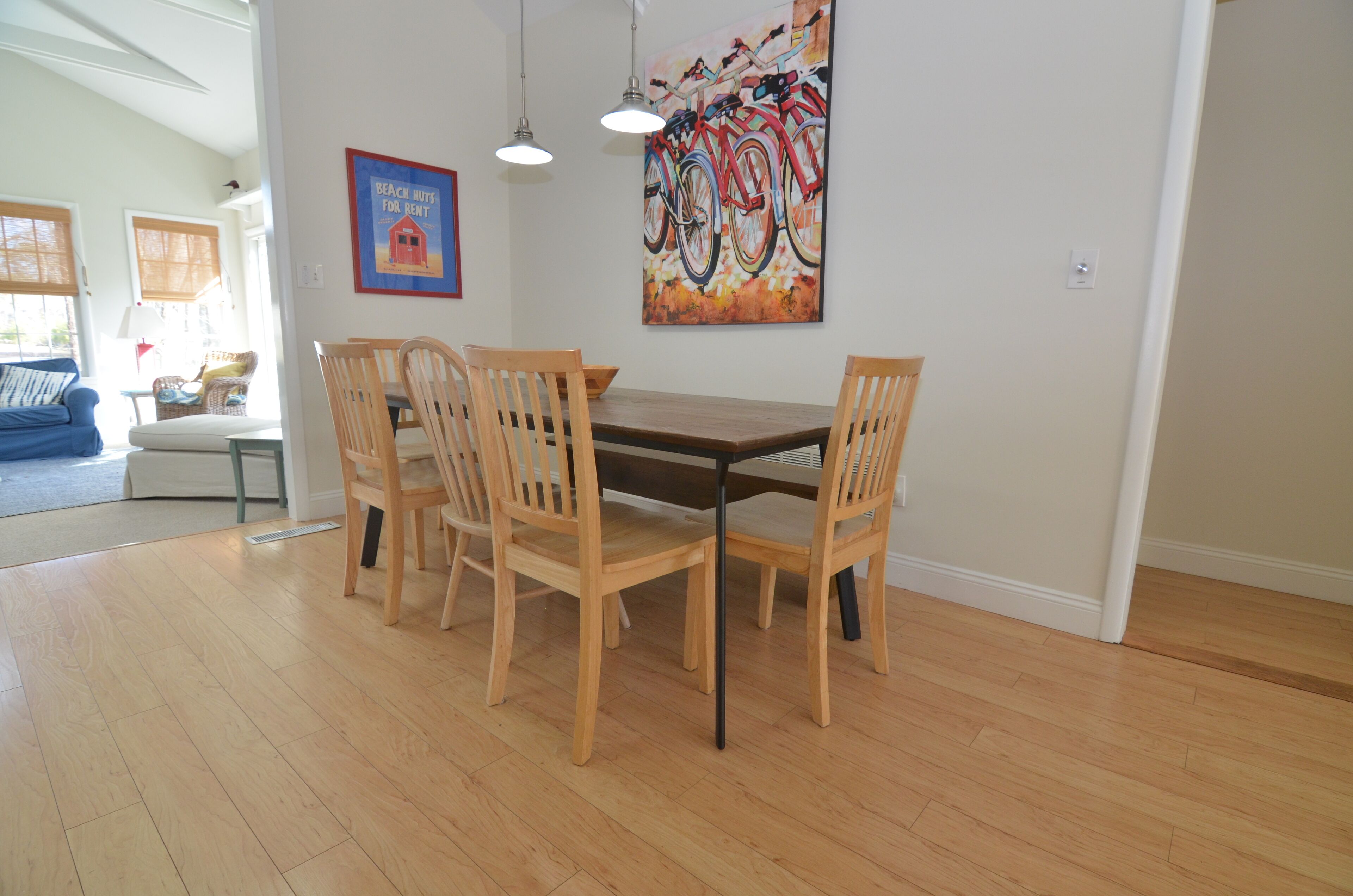 Un comedor con una mesa y sillas de madera, un cuadro de bicicletas y un cartel enmarcado en la pared.