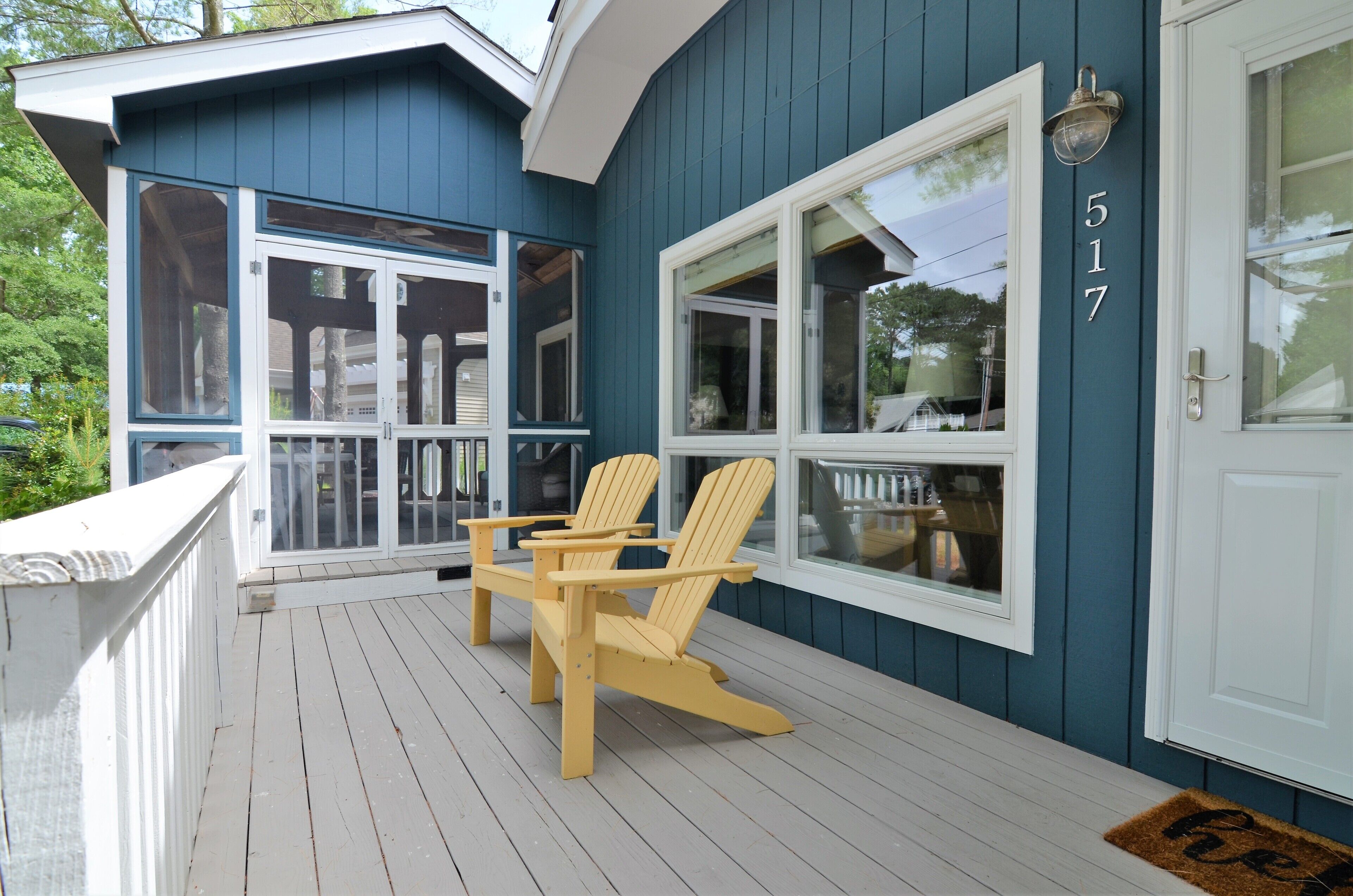 A blue house with a number 517 on the door, a porch with two wooden chairs, and a white railing.