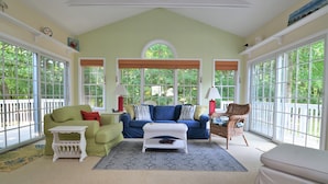 A cozy living room with a green couch, a blue sofa, and a white ottoman. There are two windows with blinds, a white side table, and a patterned rug. - 4 Bedroom, Community Pool!  517 Doral Drive, Bethany West (Bethany Beach)
