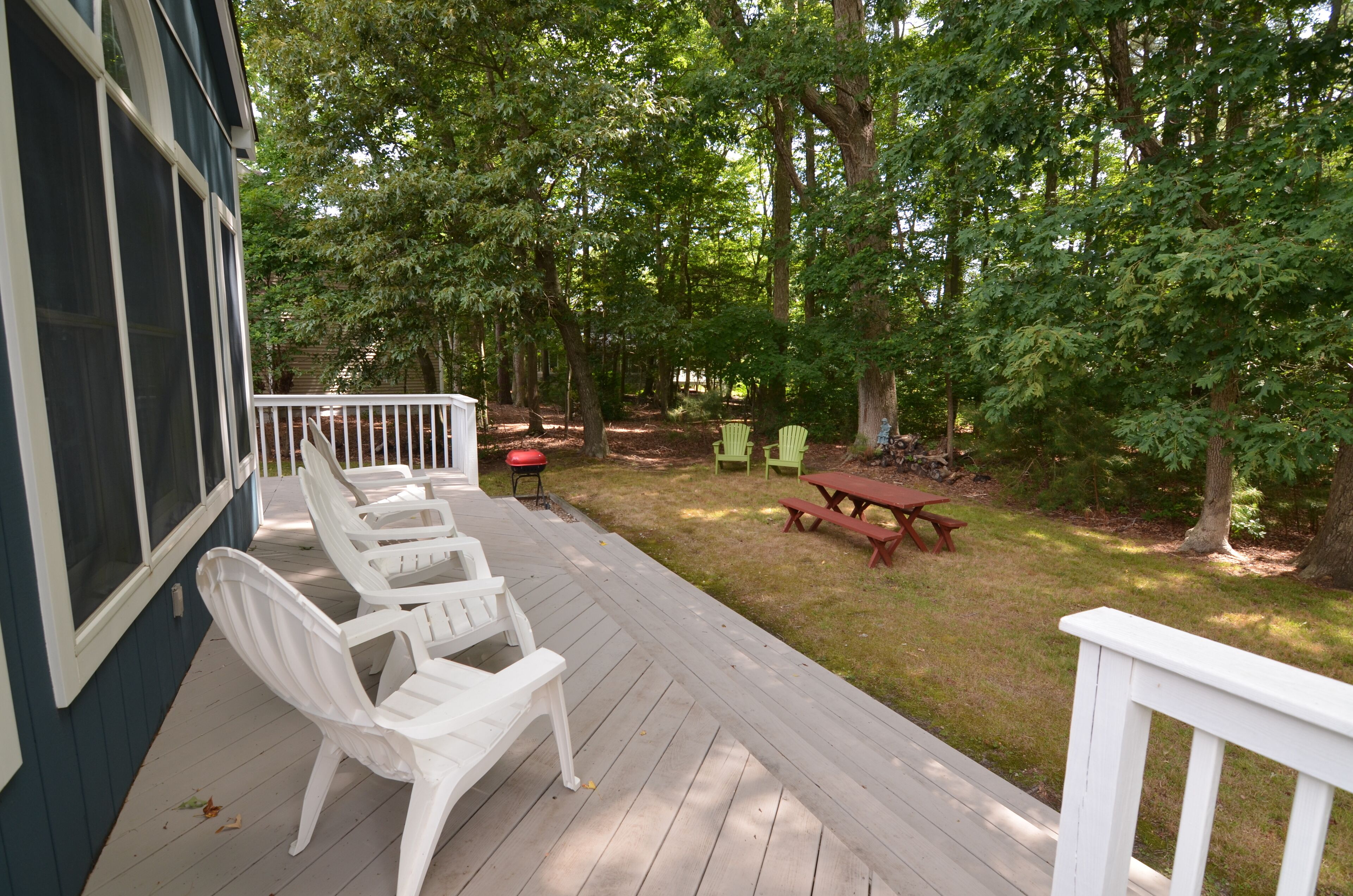 A wooden deck with white chairs and a picnic table, surrounded by trees.