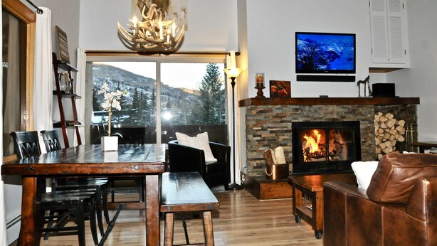 A cozy living room with a fireplace, a dining area with a large window, and a television mounted on the wall.