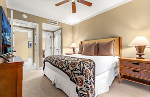Een hotelkamer met een bed, nachtlampen, een nachtkastje van hout, een plafondventilator en een deur die naar een andere kamer leidt.