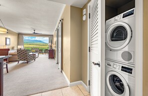 Een hotelkamer met uitzicht op een groen landschap, een zithoek met een tafel en stoelen, en een gestapelde wasmachine en droger.