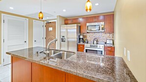 Eine moderne Küche mit Granit-Arbeitsplatten, Edelstahlgeräten, Holzschränken und Pendelleuchten.