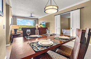 Un coin repas avec une table en bois dressée pour quatre personnes, un ventilateur de plafond et une vue sur l’extérieur.