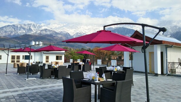 An outdoor seating area with tables and chairs, red umbrellas, and a mountainous backdrop. - D'Polo Club And Spa Resort, Dharamshala (Dharamshala)