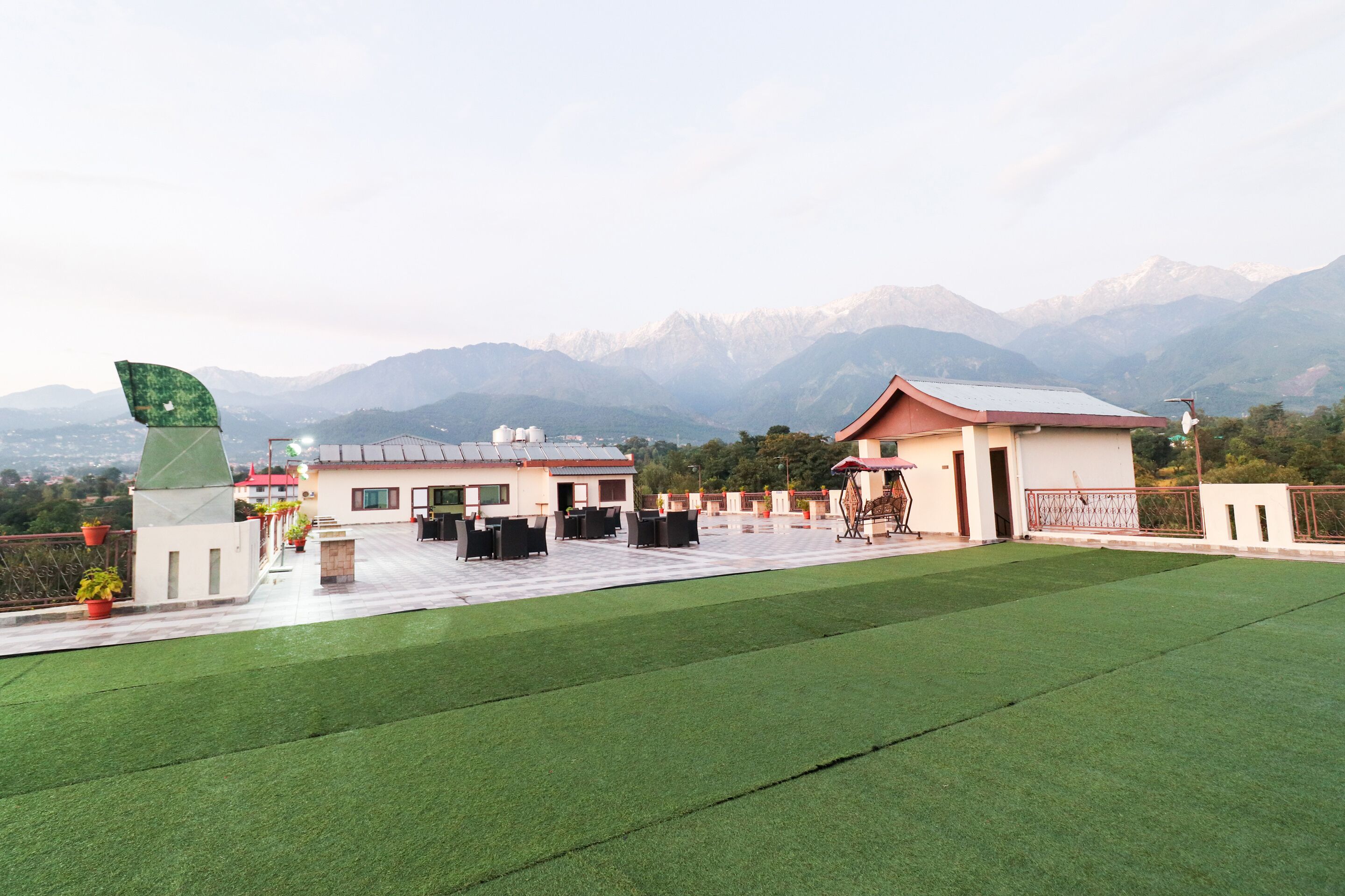 A rooftop terrace with artificial grass, outdoor seating, and a view of mountains.