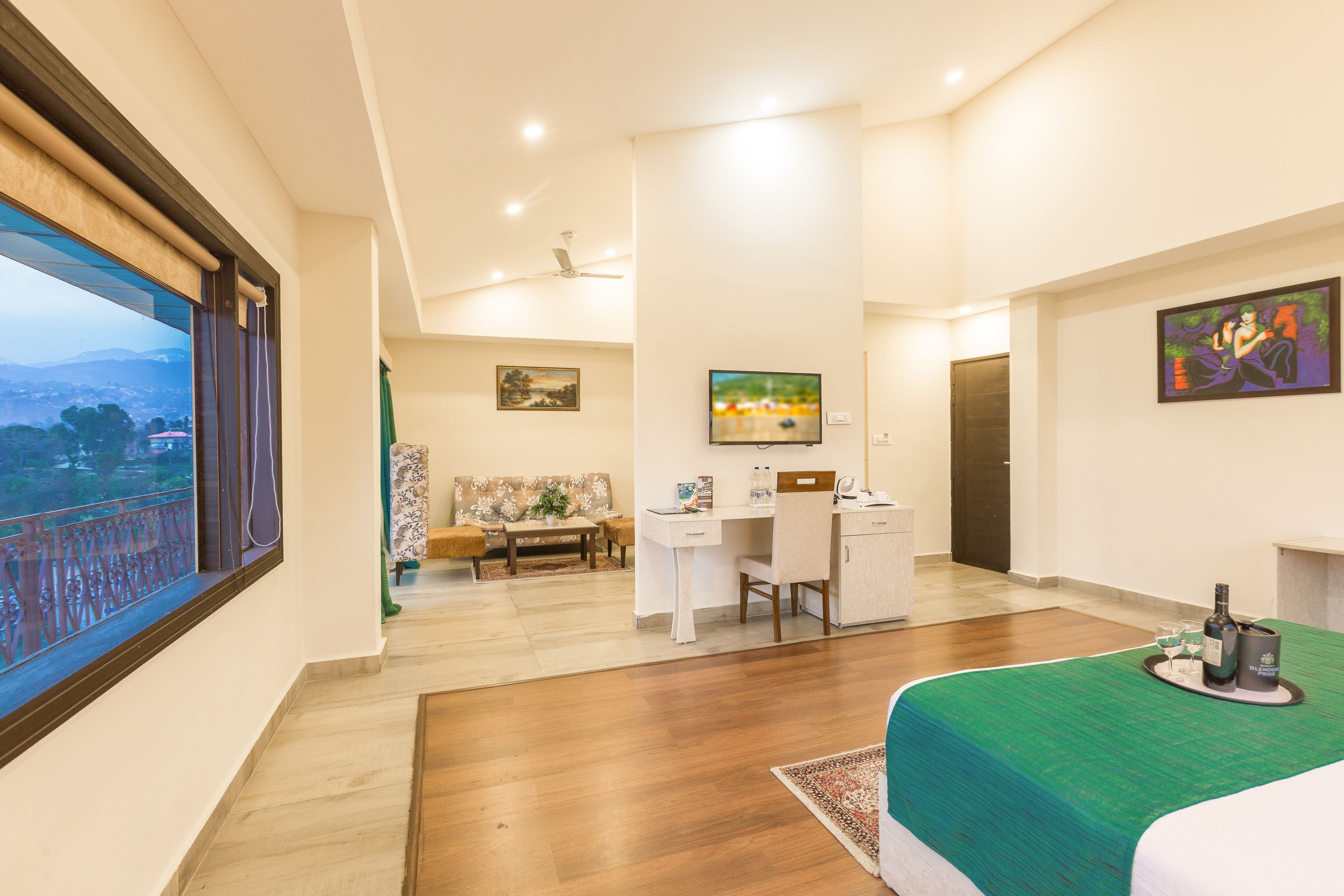 Habitación de hotel con una cama grande, un escritorio, una silla, un sofá, un televisor y un balcón con vistas a las montañas.
