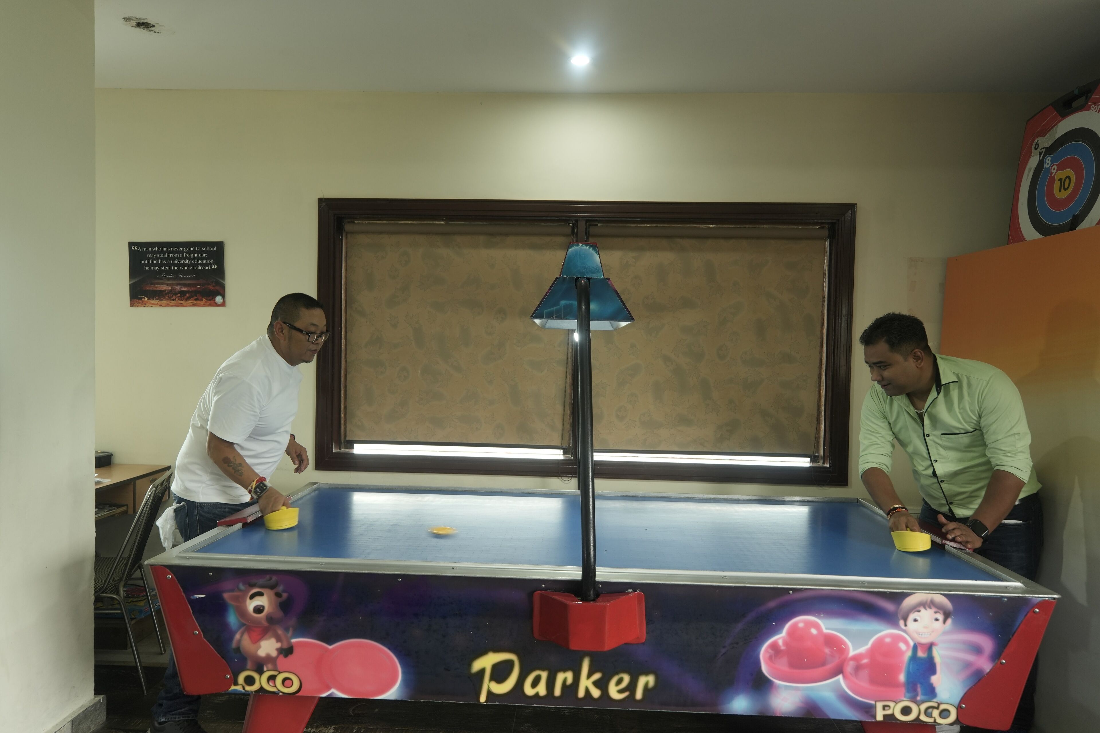 Una mesa de ping pong con los nombres "Parker" y "Poco" escritos, dos hombres jugando y un blanco en la pared.