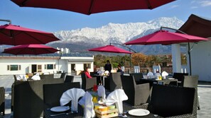 Espace extérieur aménagé avec des parasols rouges, des tables dressées pour le repas, et une vue sur les montagnes en arrière-plan.