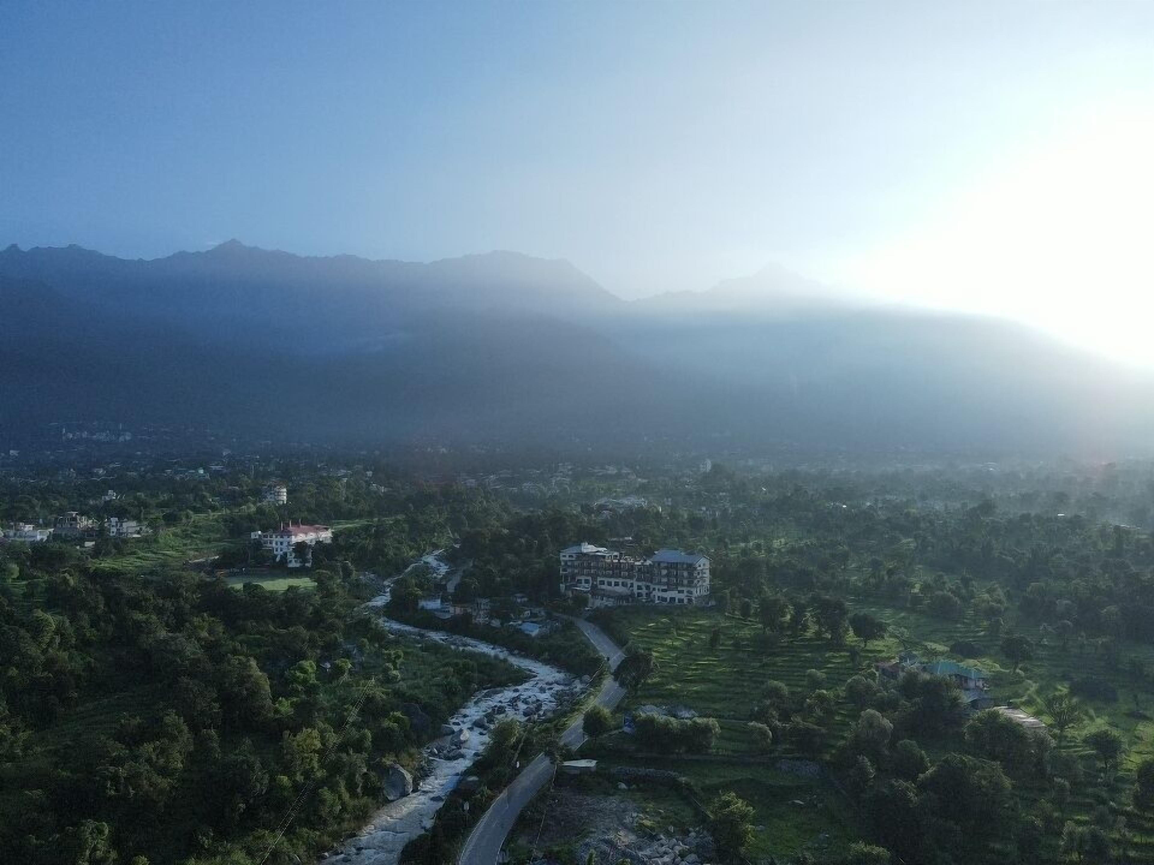 A mountainous landscape with a river, buildings, and greenery.